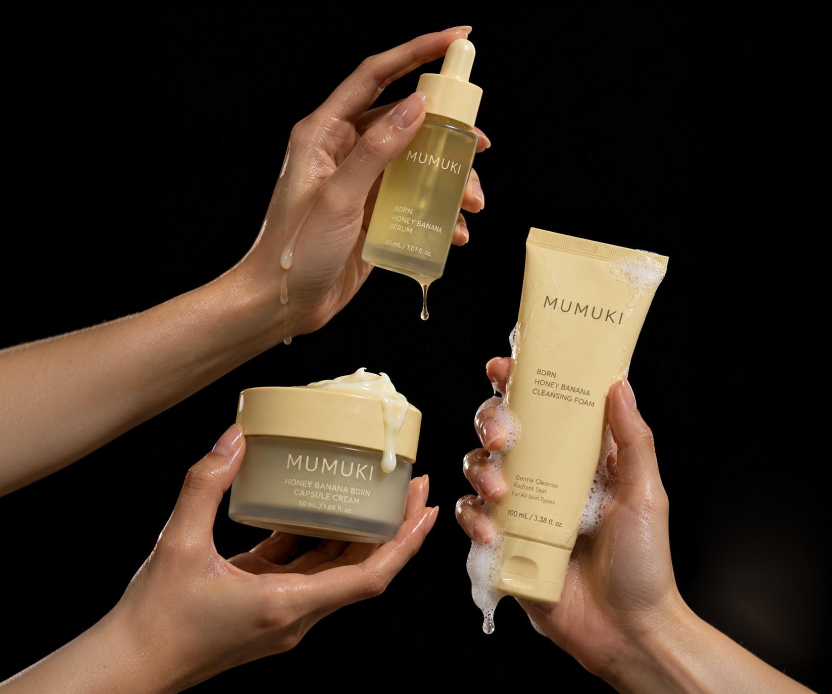MUMUKI skincare products held by hands against a black background